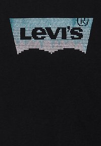 T-shirt noir avec un design dégradé de strass formant le logo Levi's, avec des couleurs bleues et blanches en haut.