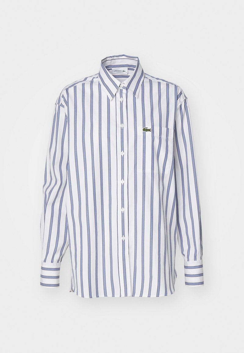 Chemise blanche à manches longues avec des rayures verticales bleues, une poche sur la poitrine et un logo brodé vert sur la poche.