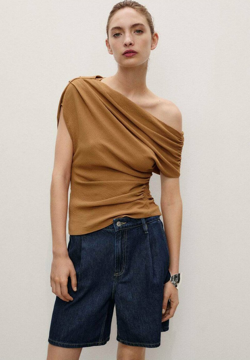 Top marron à épaules dénudées avec des détails froncés, associé à un short en denim foncé. Texture de tissu lisse et coupe ajustée avec des coutures visibles.