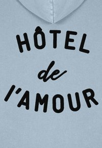 Světle modrá mikina s kapucí, na které je vyšité text "HÔTEL de l'amour" černou přízí, s regulovatelnou kapucí a měkkou texturou.