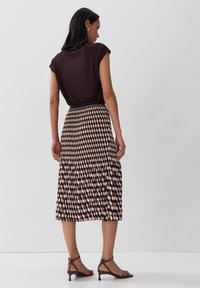 Top corto a maniche corte di colore marrone scuro abbinato a una gonna midi plissettata con un motivo geometrico in rosso, crema e nero, e sandali con le fasce.