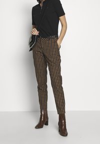 Svart polo skjorta, bruna rutiga slim-fit byxor och bruna klackstövlar. Svart axelväska med silverdetaljer.