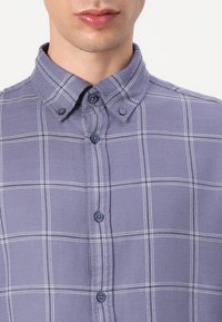 Camicia a quadri grigia e bianca, con colletto classico, due bottoni frontali e un tessuto testurizzato con una finitura morbida.