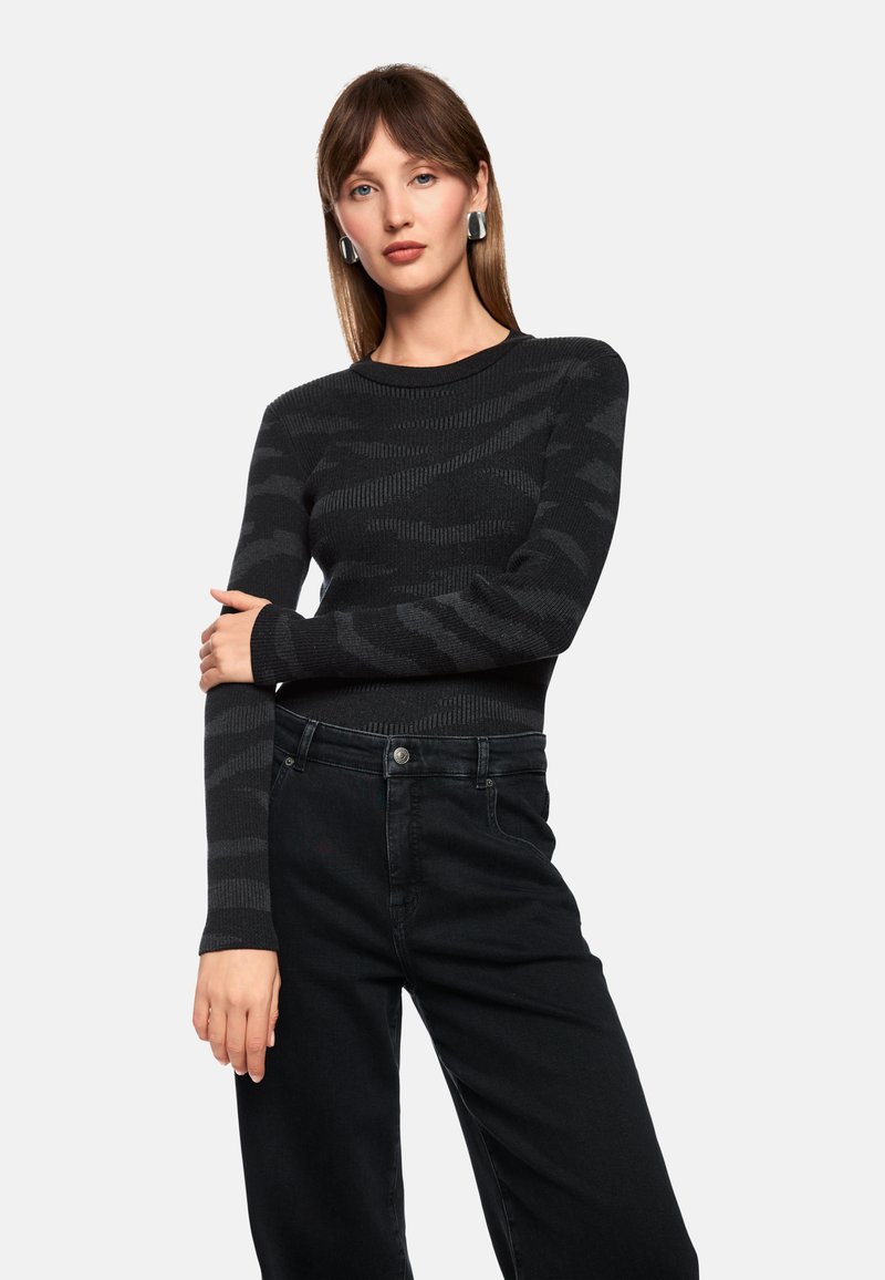 Black ribbed sweater with a subtle camo pattern; fitted design, long sleeves. Paired with high-waisted black jeans, featuring a button closure.