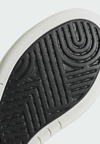 Sole di scarpa in gomma nera con un motivo testurizzato di scanalature e creste; una bordatura bianca corre lungo il perimetro.