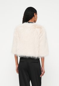 Valge kunstkarusnahast lühike jakk kolmeveerandvarrukatega, pehme ja karvane tekstuur, elegantse musta vöökohaga.