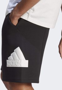 Mustat shortsit, jotka on valmistettu pehmeästä kankaasta, sisältävät näyttävän valkoisen Adidas-logon ja erottuvat sivutaskut toiminnallisuuden vuoksi.