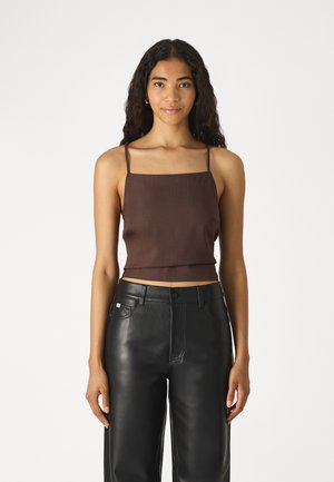 Brown crop top with thin straps, featuring a square neckline and a smooth texture. Paired with high-waisted black leather pants.