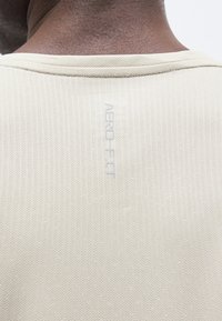 Gros plan du haut du dos d'une personne à la peau foncée portant une chemise beige texturée avec « AERO-FIT » imprimé verticalement sous l'encolure.