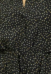 Černé šaty s malými bílými a hnědými vzory ve tvaru semínek, s knoflíky vpředu a tkaným páskem v pase.