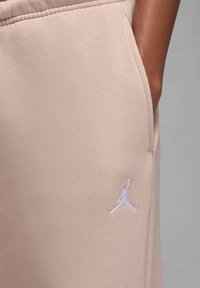 Beige joggingbroek gemaakt van zacht stof, voorzien van een zijzak en een wit geborduurd Jumpman-logo op de onderkant van de linker bovenbeen.