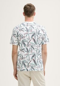 Camiseta blanca de manga corta con un patrón de hojas verdes y rosas. Material de algodón con un ajuste regular y cuello redondo.