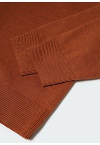 Manches de pull en tricot couleur rouille avec poignets et ourlet côtelés sur un fond pâle, montrant la texture et les détails du tissu.