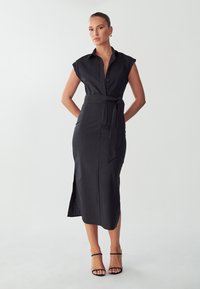 Vestido negro de camiseta con mangas cortas, cintura ceñida, abertura lateral y cierre de botones en la parte delantera. Fabricado con una tela suave y con un silueta ajustada.