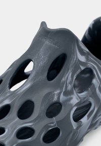 Chaussures grises au design perforé unique, présentant des lignes fluides et lisses avec des tailles de trous variées, fabriquées dans un matériau léger.