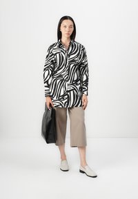 Camicia a righe bianco e nero con maniche lunghe, abbinata a pantaloni cropped beige e scarpe slip-on chiare; borsa nera.