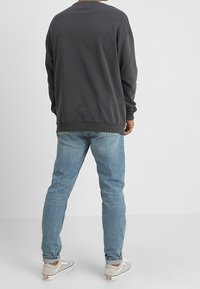 Šedá mikina s dlouhými rukávy, žebrovanými manžetami a lemem; v kombinaci se světle modrými džínami a šedými botami; jednoduchý design bez viditelných vzorů nebo log.