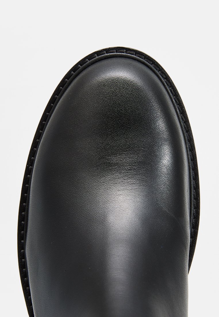 Schwarze, polierte Lederstiefelspitze mit genähtem Rahmen auf weißem Hintergrund.