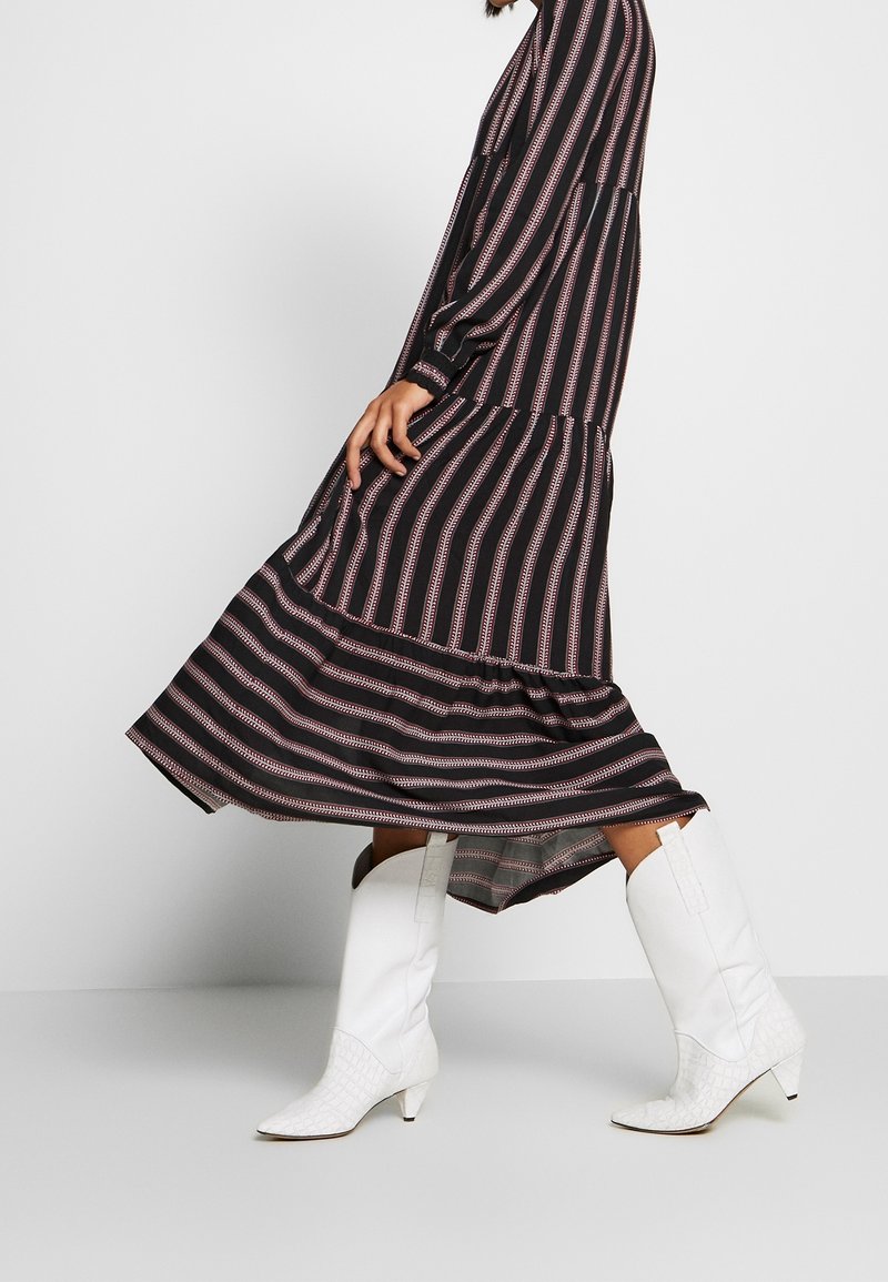 Černobíle pruhované šaty s červenými akcenty, vrstvený design, dlouhé rukávy. V kombinaci s bílými koženými cowboyskými botami s texturovaným povrchem.