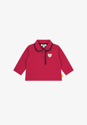 Czerwona koszulka dla niemowląt z długim rękawem, z kołnierzykiem wykończonym na czarno, dwoma czarnymi guzikami i małą beżową łatką z niedźwiadkiem na klatce piersiowej.