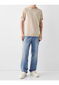 Beige cotton t-shirt paired with light blue straight-leg denim jeans. Worn with white sneakers, showcasing a simple, casual style.