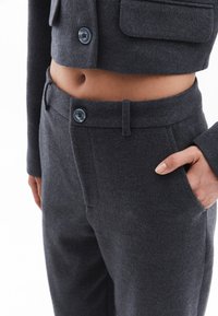 Donkergrijze cropped jas en bijpassende hoge broek, beide gemaakt van zachte stof met blauwe knopen en zijzakken.