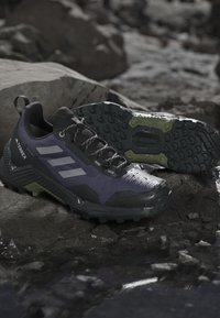 Svarta och lila trailrunning skor med en strukturerad ovandel, formar hälen och aggressiv mönstring på sulan för bra grepp på olika terränger.