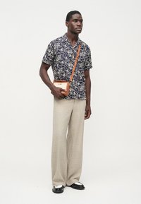 Modrá námornícka košeľa s krátkym rukávom a bielym kvetinovým vzorom, béžové široké nohavice a oranžová kabelka cez rameno. Čierne topánky s bielymi detailmi.