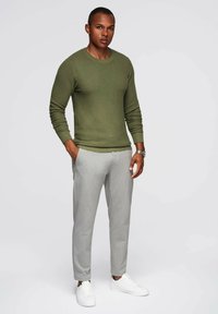 Olijfgroen geribd sweater met ronde hals, gecombineerd met lichtgrijze broek en witte sneakers, met een gladde textuur en slanke pasvorm.