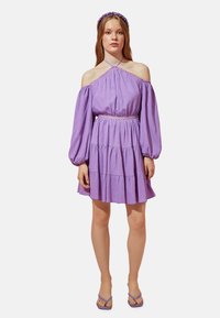 Lila schulterfreies Kleid mit Ballonärmeln, geschichteter Rock, strukturiertes Gewebe und Spitzenverzierungen. Getragen mit passenden Accessoires.