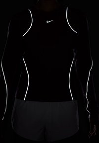 Dlouhý rukáv sportovního trička v tmavě vínové barvě s reflexními bílými detaily podél švů. Na prsou se nachází logo Nike, hladká textura.