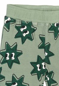 Leggings verzi cu un model repetitiv de stele cu ochi prietenoși, realizate dintr-un material moale și dotate cu un elastic ribbat pentru confort.
