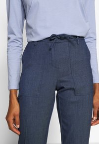 Pantalon en tissu bleu marine tissé avec une coupe décontractée, doté d'une taille à cordon de serrage et de deux poches plaquées à l'avant. Texture lisse.