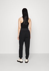 Svart linne kombinerat med svarta joggerbyxor, som har elastiskt midjeband och uppvikta anklar. Modellen bär ljusa skor.