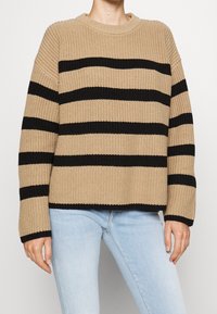Beige gebreide sweater met zwarte horizontale strepen, ronde halslijn en lange mouwen, met een geribbelde textuur en een ontspannen pasvorm.