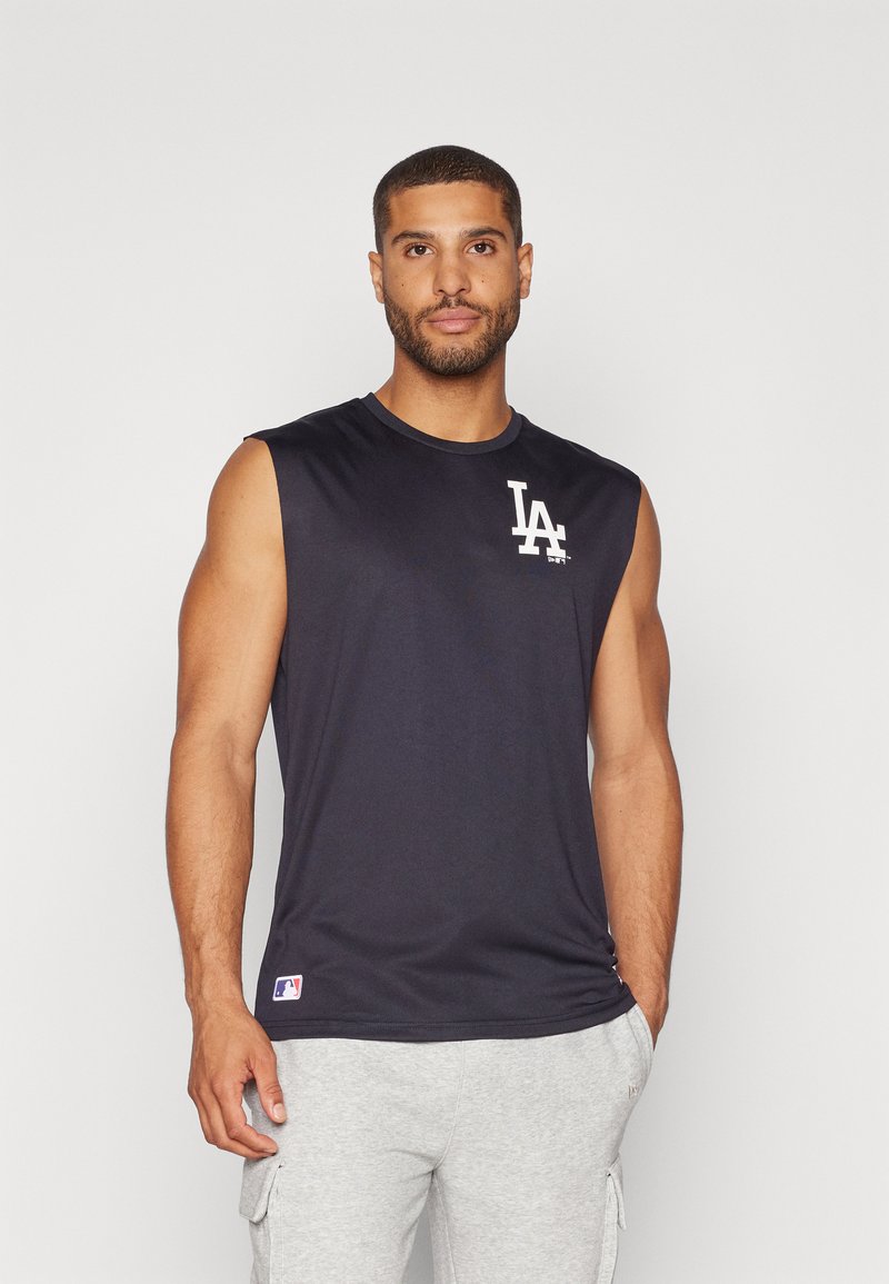 Camiseta atlética sin mangas de color azul marino con un escote redondo y el logo de LA en el pecho. Hecha de una tela suave y transpirable. Combinada con pantalones cortos de color gris claro.
