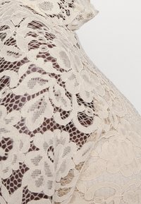Ivory lace fabric features intricate floral patterns and open weave, showcasing a delicate and textured surface with a soft drape.