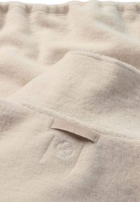 Manta color crema con un material de vellón suave y texturizado. Cuenta con una pequeña etiqueta de tela y un diseño sutil en relieve.