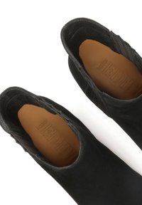 Melni zamšaini potīšu zābaki ar gludu, noapaļotu purngalu, mīkstu iekšējo odere un smalku teksturētu apdari gar malām.