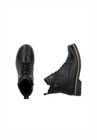 Bottines en cuir noir avec bout rond, lacées à l'avant, œillets rouges et fermeture éclair sur le côté. Semelle en caoutchouc texturé avec accents marron.