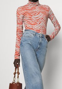 Långärmad polokrage med orange och vita vågiga ränder, matchad med högmidjade ljusblå denimjeans och en brun handväska.