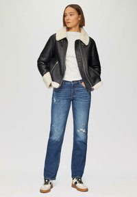 Veste en cuir noir avec un col en shearling blanc, associée à un jean en denim délavé bleu clair et des baskets blanches avec des accents noirs.