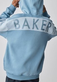 Hellblauer Hoodie mit einem großen "BAKER"-Grafik in dunklerem Blau auf der Rückseite. Glatte Textur mit gerippten Bündchen und Saum.