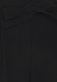 Svarta byxor med en rosettknuten bälte, med subtila sömmar och en slät yta. Fickor synliga på framsidan. Skräddarsydd design.