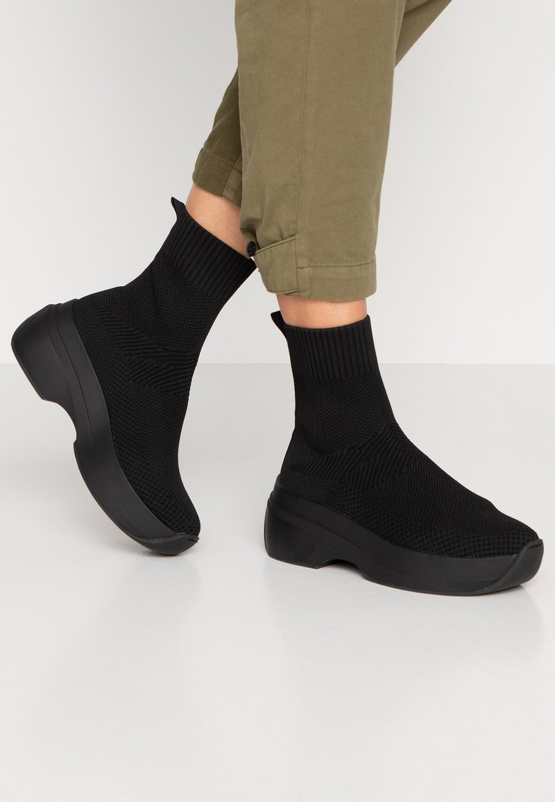 Černé pletené sock sneakers s texturovaným povrchem, polstrovanou podrážkou a elegantním siluetou. Obsahují žebrovaný manžet a minimalistický design.