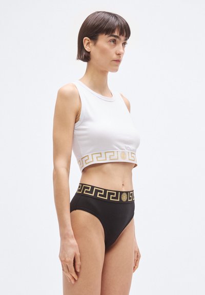 Άσπρο κοντό τοπ με χρυσό μοτίβο ελληνικού κλειδιού και μαύρο σλιπ μέσης με χρυσή αντίστοιχη ζώνη. Λείο ύφασμα, μινιμαλιστικός σχεδιασμός.