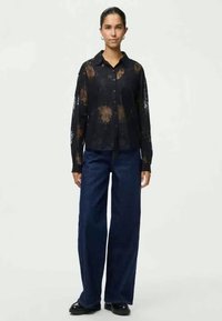 Juoda, puspermatoma marškiniai su mygtukais, gėlėmis, ilgomis rankovėmis ir apykakle, derinama su tamsiai mėlynomis plačiomis kelnėmis.