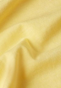 Tessuto giallo con una consistenza morbida e rigata, caratterizzato da pieghe delicate e superfici lisce che riflettono la luce.