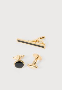 Μανικετόκουμπα σε χρυσό τόνο και κλιπ γραβάτας με μαύρες λεπτομέρειες. Μανικετόκουμπα: στρογγυλά με υφή στην άκρη. Κλιπ γραβάτας: κομψό, ορθογώνιο με μαύρο ένθετο.