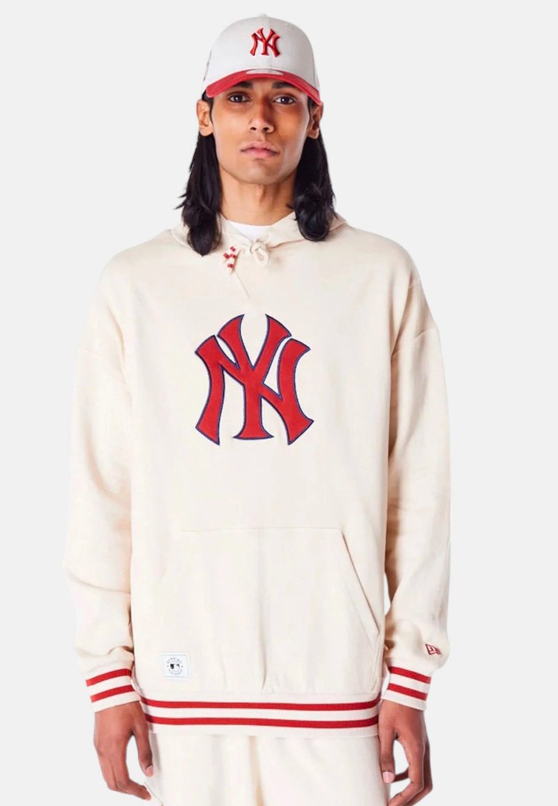 Felpa crema con logo NY rosso e strisce rosse sulle maniche e sul bordo. Abbinata a un cappellino bianco con logo NY rosso.